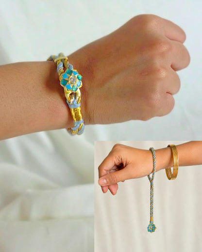 A 925 Silver rakhi bracelet with turquoise blue and golden woven threads is shown worn on a person's wrist. Lumba Rakhi for Bhabhi crafted in 925 sterling silver.