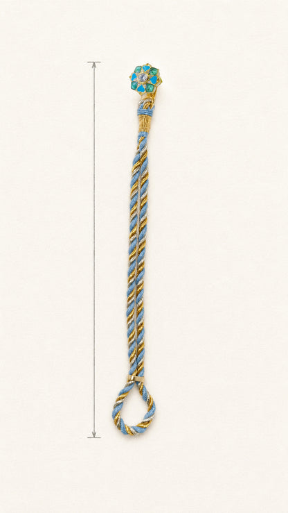 A braided rakhi bracelet with a floral motif and a loop at the bottom, shown on a plain light background with a vertical measurement marker along the left side.