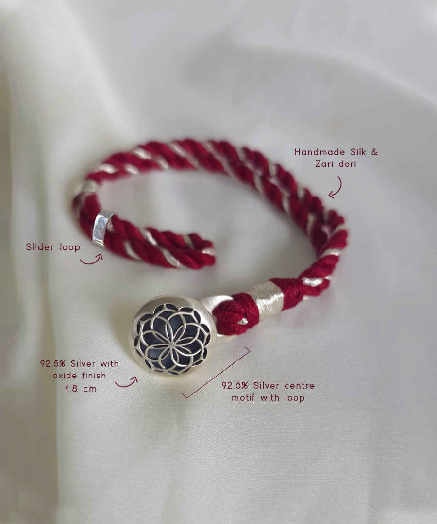 A handmade red silk and Zari dori bracelet with a silver -sacred geometry charm