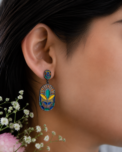 Model wearing handcrafted drop earrings in 925 sterling silver, black rhodium finish with colorful enamel detailing.